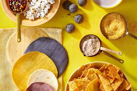 Assortment of corn products like flour, tortillas, chips and popcorn in bowls on yellow background.